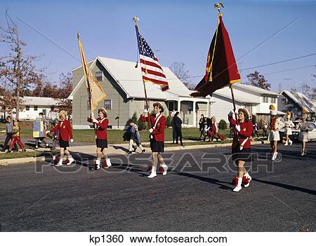 Stock Image - 1960s high school band marching color guard leading halloween parade down suburban street. Fotosearch