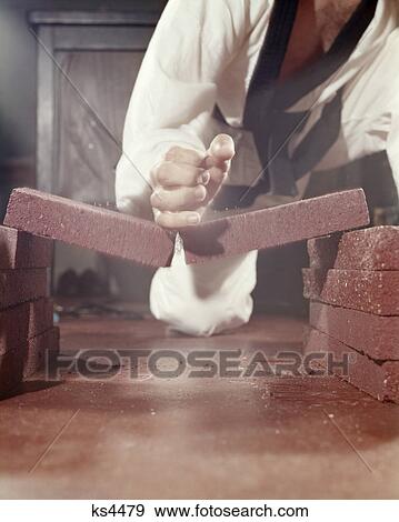 Stock Photo - 1960s man hand breaking brick tile with judo karate chop strong strength. Fotosearch