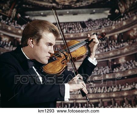 Stock Image - 1960s man playing the violin in concert hall. Fotosearch