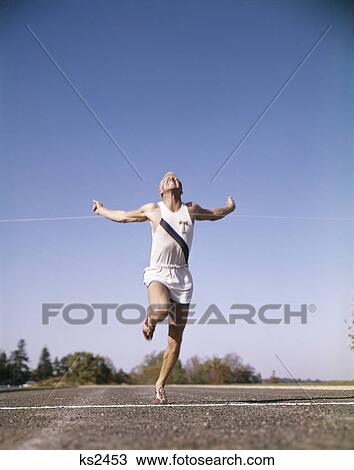 Stock Image - 1960s man winning race running through tape at finish line. Fotosearch
