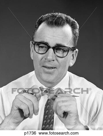 Stock Photograph - 1960s portrait of businessman wearing glasses holding pencil in both hands thoughtful pensive expression. Fotosearch