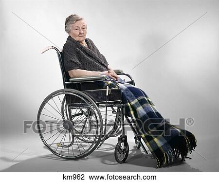 Stock Image - 1960s sad senior woman sitting in wheelchair shawl on shoulders and a plaid lap blanket. Fotosearch