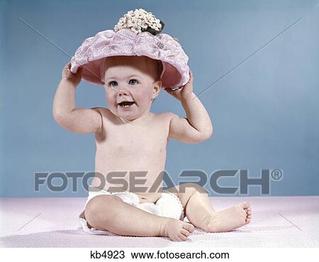 Stock Image - 1960s smiling baby girl wearing diaper and large pink hat. Fotosearch