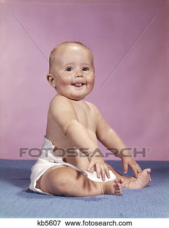 1960s smiling baby wearing cloth diaper sitting on blue blanket sticking out tongue View Large Photo Image Stock Photo - 1960s smiling baby wearing cloth diaper sitting on blue blanket sticking out tongue. Fotosearch