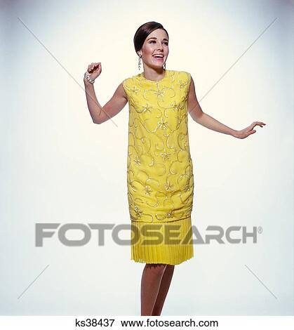 Stock Photo - 1960s smiling brunette woman modeling yellow sequined cocktail dress clothes. Fotosearch