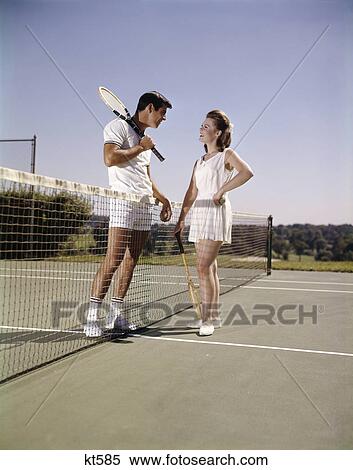 1960s smiling couple man woman standing on opposite sides of net tennis court holding rackets recreation View Large Photo Image Stock Photography - 1960s smiling couple man woman standing on opposite sides of net tennis court holding rackets recreation. Fotosearch