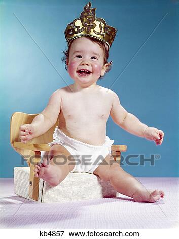 1960s smiling happy baby wearing crown sitting on booster seat chair View Large Photo Image Stock Photo - 1960s smiling happy baby wearing crown sitting on booster seat chair. Fotosearch