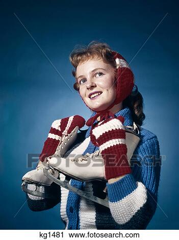 1960s smiling woman wearing red mittens ear muffs and blue sweater holding ice skates looking up winter studio red hair View Large Photo Image Stock Image - 1960s smiling woman wearing red mittens ear muffs and blue sweater holding ice skates looking up winter studio red hair. Fotosearch
