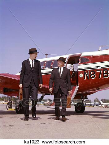1960s two businessmen in suits and hats carrying briefcases walking from a small twin prop business airplane talking View Large Photo Image Stock Image - 1960s two businessmen in suits and hats carrying briefcases walking from a small twin prop business airplane talking. Fotosearch