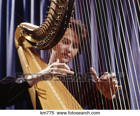 Stock Photography - 1960s woman playing harp plucking strings. Fotosearch