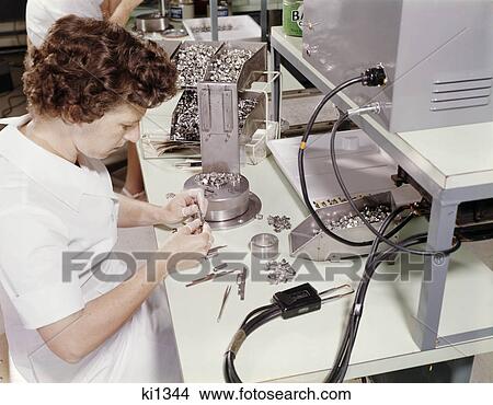 Picture - 1960s woman worker assembling television color gun at television tube factory. Fotosearch