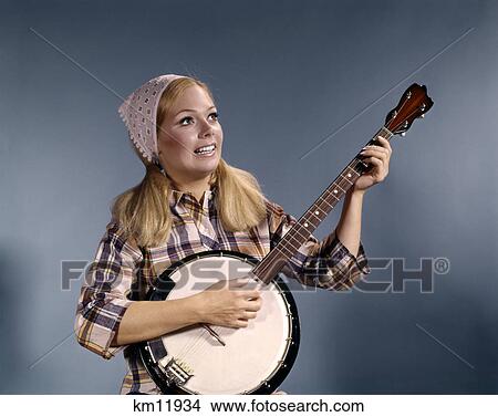 Picture - 1960s young blond woman playing banjo wearing plaid shirt. Fotosearch