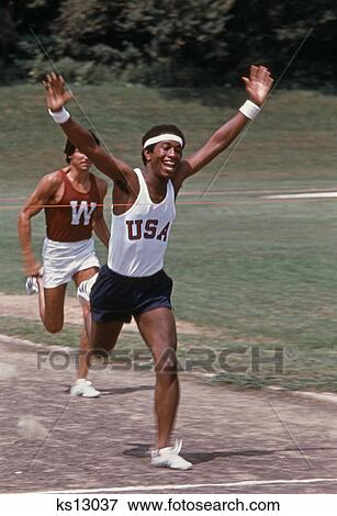 1970s 2 runners african-american man breaking tape at finish line View Large Photo Image Stock Photo - 1970s 2 runners african-american man breaking tape at finish line. Fotosearch