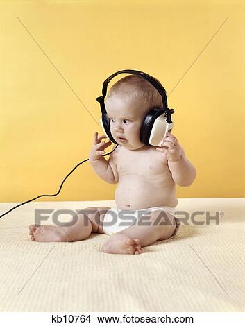 1970s baby wearing diaper listening to oversized headphones yellow background View Large Photo Image Picture - 1970s baby wearing diaper listening to oversized headphones yellow background. Fotosearch