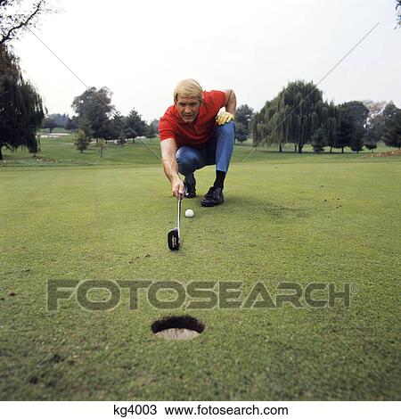 Stock Image - 1970s blond man playing golf crouching lining up shot on green course exercise recreation sports. Fotosearch