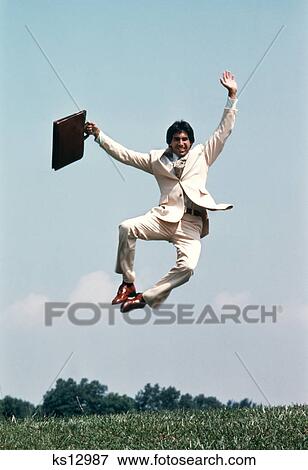 1970s businessman holding briefcase jumping in air clicking heels together View Large Photo Image Stock Photo - 1970s businessman holding briefcase jumping in air clicking heels together. Fotosearch