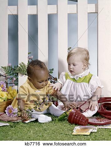 1970s caucasian and african american baby girls playing together with flowers and plastic gardening tools View Large Photo Image Stock Photograph - 1970s caucasian and african american baby girls playing together with flowers and plastic gardening tools. Fotosearch