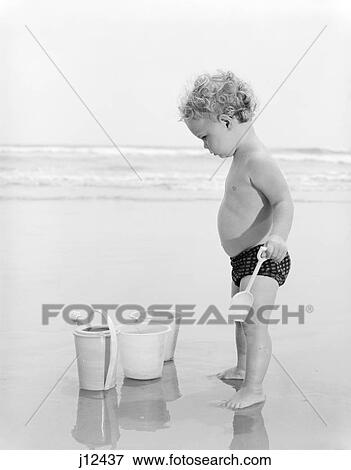 1970s child toddler standing in sand water bucket shovel View Large Photo Image Stock Photo - 1970s child toddler standing in sand water bucket shovel. Fotosearch