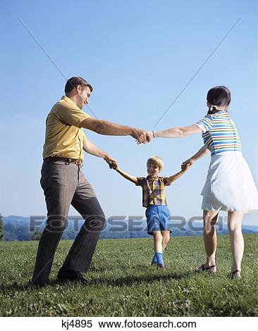 Stock Photography - 1970s family mother father boy playing ring around roses holding hands circle man woman child. Fotosearch