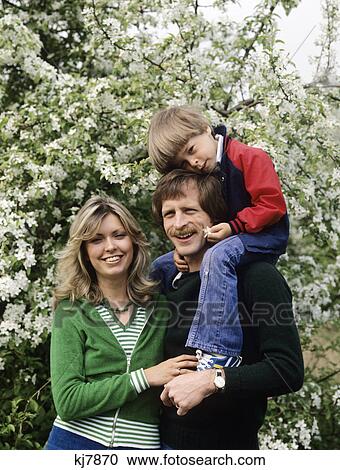 1970s family portrait outdoors by tree boy sitting on fathers shoulders View Large Photo Image Stock Image - 1970s family portrait outdoors by tree boy sitting on fathers shoulders. Fotosearch