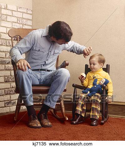 1970s father sitting in rocking chair next to son in small chair eating an apple View Large Photo Image Stock Photography - 1970s father sitting in rocking chair next to son in small chair eating an apple. Fotosearch
