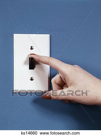 Stock Image - 1970s female hand with finger flipping off light switch. Fotosearch