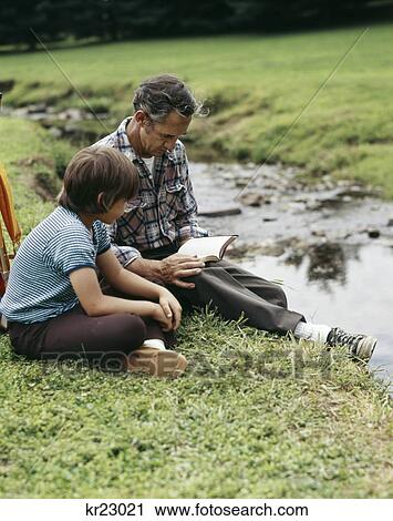 1970s man and boy father son outdoor by stream reading bible View Large Photo Image Stock Image - 1970s man and boy father son outdoor by stream reading bible. Fotosearch