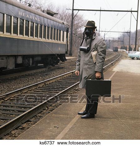 Stock Photo - 1970s man commuter wearing gas mask carrying briefcase waiting on train platform. Fotosearch