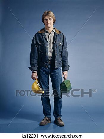 Stock Image - 1970s man construction worker hard hat lunch box denim jacket. Fotosearch