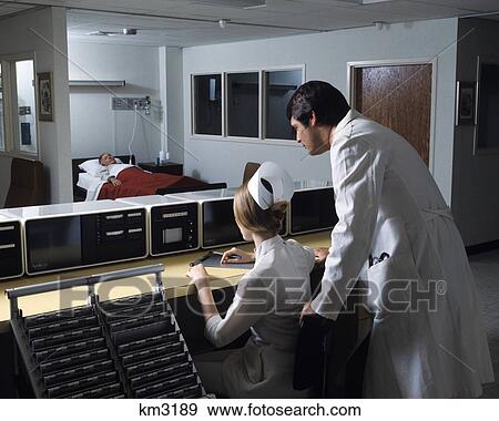 Stock Photo - 1970s man doctor woman nurse observing male patient checking vital signs on monitors in hospital icu. Fotosearch