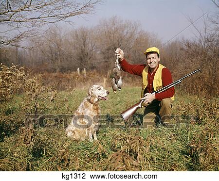 Stock Image - 1970s man with hunting dog and gun holding up brace of birds. Fotosearch
