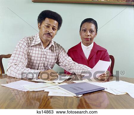 1970s middle aged african american couple man woman seated at table going over household accounts View Large Photo Image Stock Image - 1970s middle aged african american couple man woman seated at table going over household accounts. Fotosearch