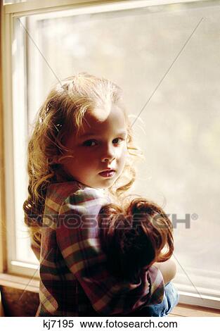 1970s sad blond girl holding doll standing by window View Large Photo Image Stock Photography - 1970s sad blond girl holding doll standing by window. Fotosearch
