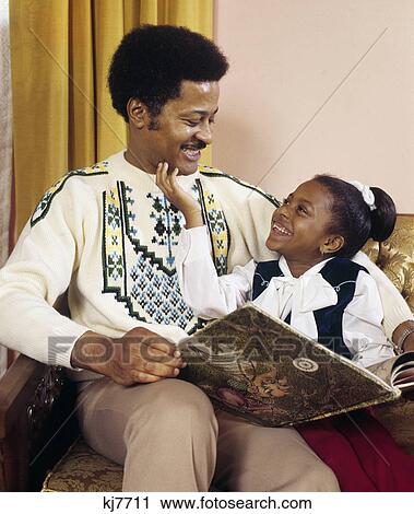 1970s smiling african american man father and daughter sitting together reading story book View Large Photo Image Stock Image - 1970s smiling african american man father and daughter sitting together reading story book. Fotosearch