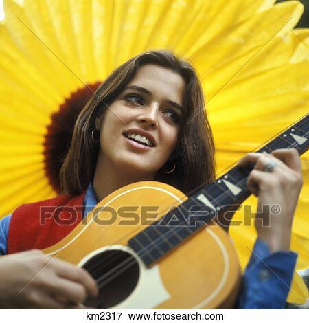 1970s smiling teenaged girl playing acoustic guitar with large yellow sunflower backdrop View Large Photo Image Stock Photo - 1970s smiling teenaged girl playing acoustic guitar with large yellow sunflower backdrop. Fotosearch