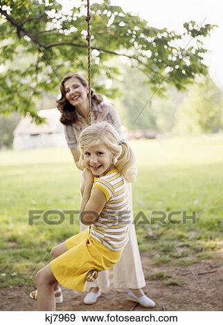 1970s smiling woman mother with girl daughter swinging playing on rope swing View Large Photo Image Stock Photo - 1970s smiling woman mother with girl daughter swinging playing on rope swing. Fotosearch