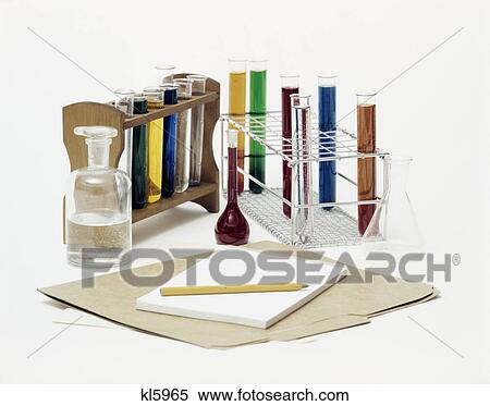 Stock Photography - 1970s still life of test tubes bottles filled with colorful liquids and folder paper tablet and pencil. Fotosearch