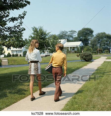 1970s teen boy and girl walking down suburban street carrying school books View Large Photo Image Stock Photo - 1970s teen boy and girl walking down suburban street carrying school books. Fotosearch