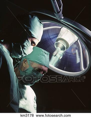 1970s two doctors surgeons wearing caps and masks under operating room light View Large Photo Image Stock Photo - 1970s two doctors surgeons wearing caps and masks under operating room light. Fotosearch