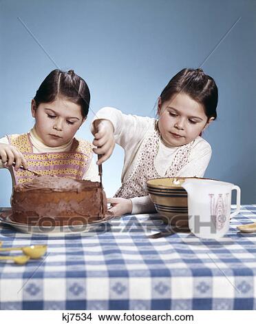 Picture - 1970s two sisters twins frosting chocolate cake baking cooking. Fotosearch