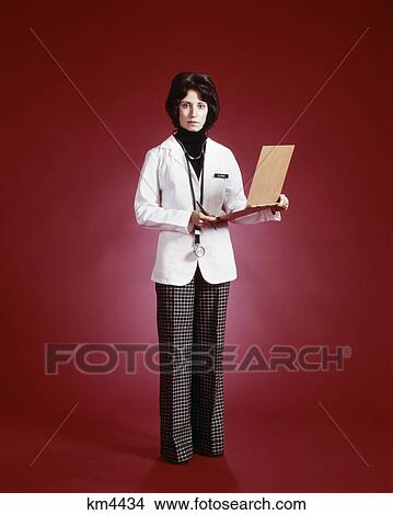 Picture - 1970s woman doctor full length portrait standing holding patient chart. Fotosearch