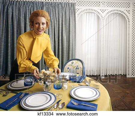 1970s woman hostess yellow tie blouse flowers on dining table blue white china dishes household home entertaining View Large Photo Image Picture - 1970s woman hostess yellow tie blouse flowers on dining table blue white china dishes household home entertaining. Fotosearch