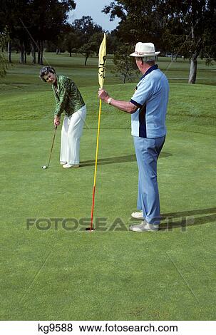 1980s senior couple playing golf woman putting on green View Large Photo Image Stock Photo - 1980s senior couple playing golf woman putting on green. Fotosearch