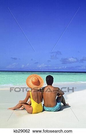 Stock Image - 1990s man and woman sitting on the beach facing the water mopion island, grenadines, west indies. Fotosearch