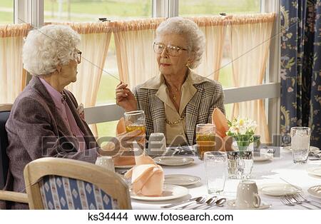 Picture - 1990s two senior women conversing while sitting in dining room of restaurant. Fotosearch