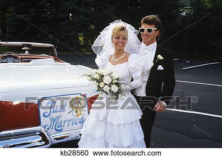 Stock Image - 1991 bride and groom standing next to vintage convertible ford car. Fotosearch