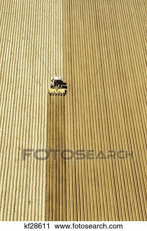 Stock Image - aerial view of farm machinery plowing fields central california. Fotosearch