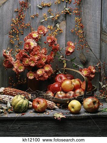 Stock Image - autumn harvest still life squash and fruits flowers and corn against barn wood. Fotosearch
