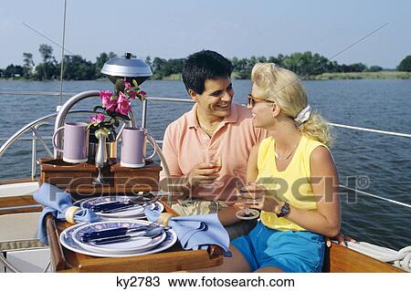 Stock Image - couple interacting in cockpit of sailboat with table setting in foreground. Fotosearch