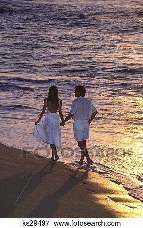 couple walking along beach at sunset by the waters edge View Large Photo Image Stock Photo - couple walking along beach at sunset by the waters edge. Fotosearch